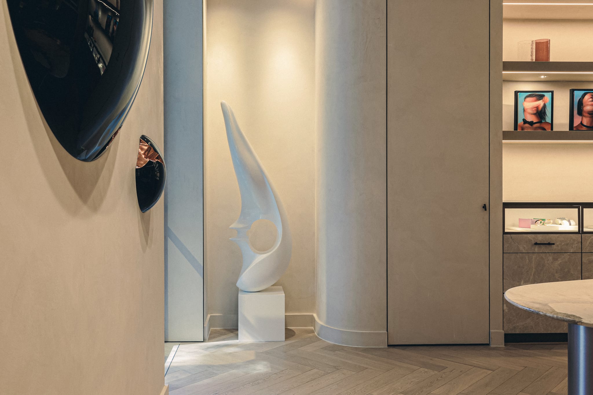 Tall white abstract sculpture on a plinth in a rendered alcove, with dark convex wall mirrors and herringbone oak flooring.