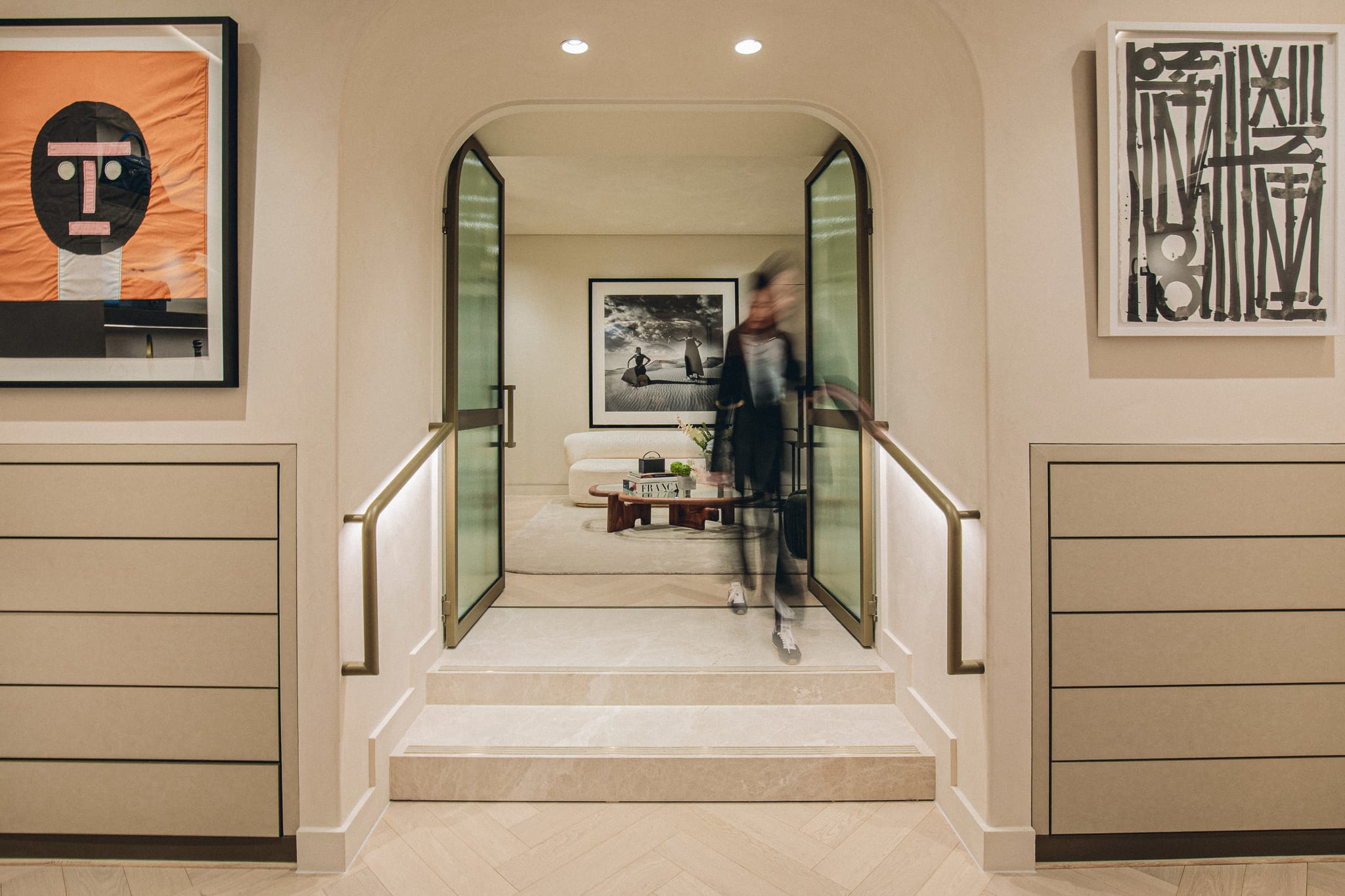 Travertine steps rise through arched brass and glass doors to a lounge, framed artworks flanking the passage in the Double Bay boutique.