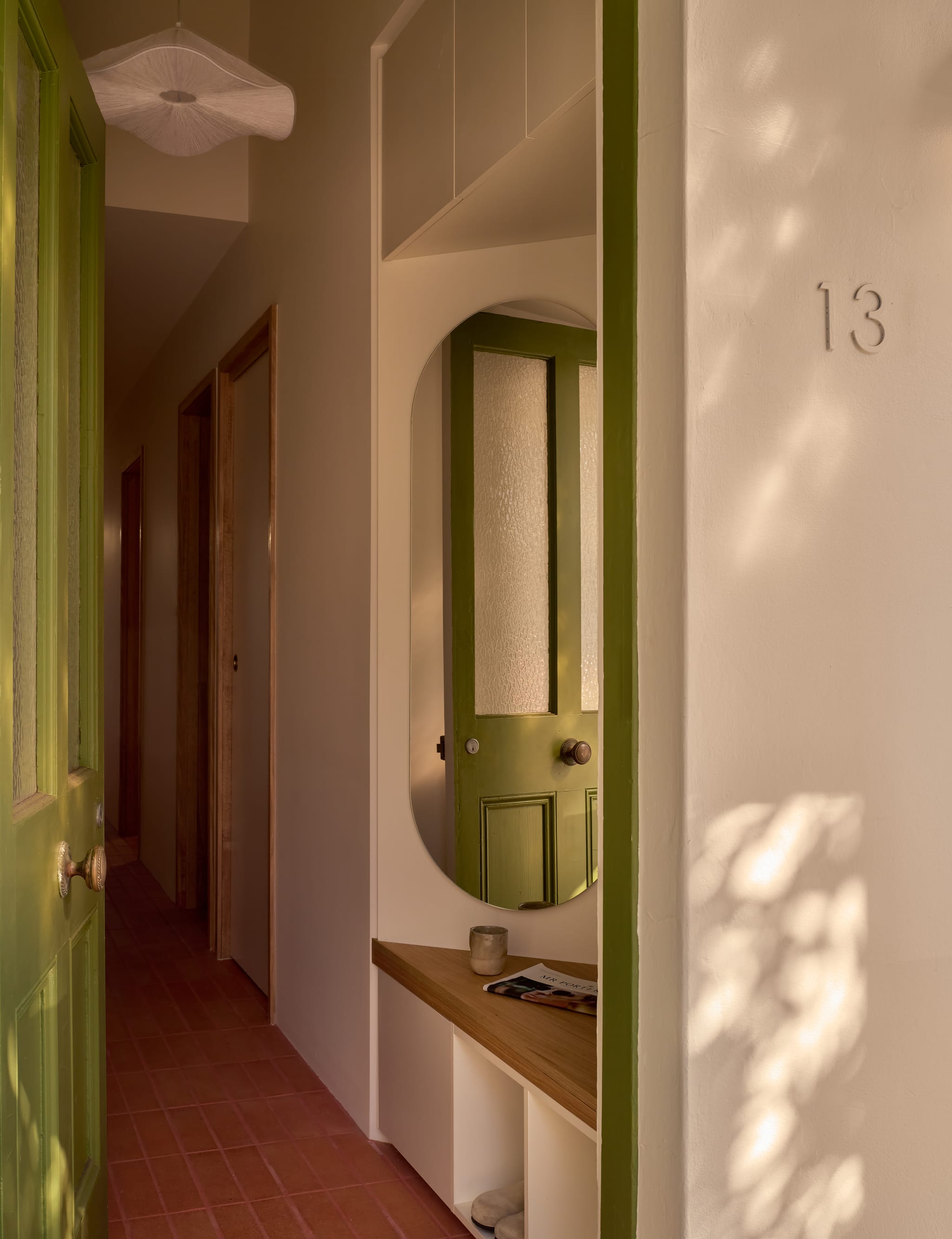 Hallway on terracotta tiles with an olive-green heritage door, a built-in oak niche and oval mirror, and 13 embossed on the rendered wall.