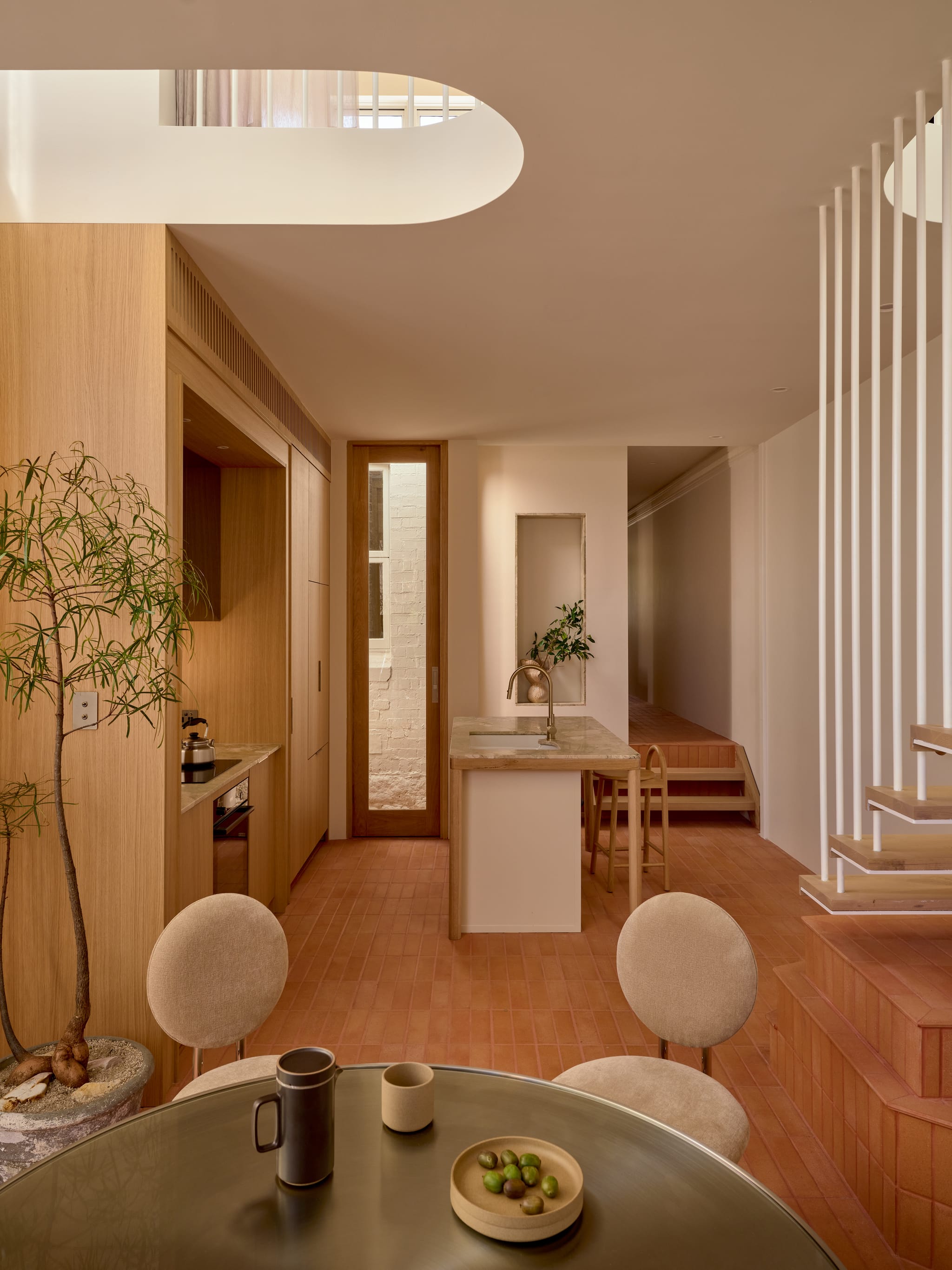 Open rear pavilion of the Birchgrove terrace: an oval skylight, floating stair, terracotta floor and a marble island beside the compact kitchen.