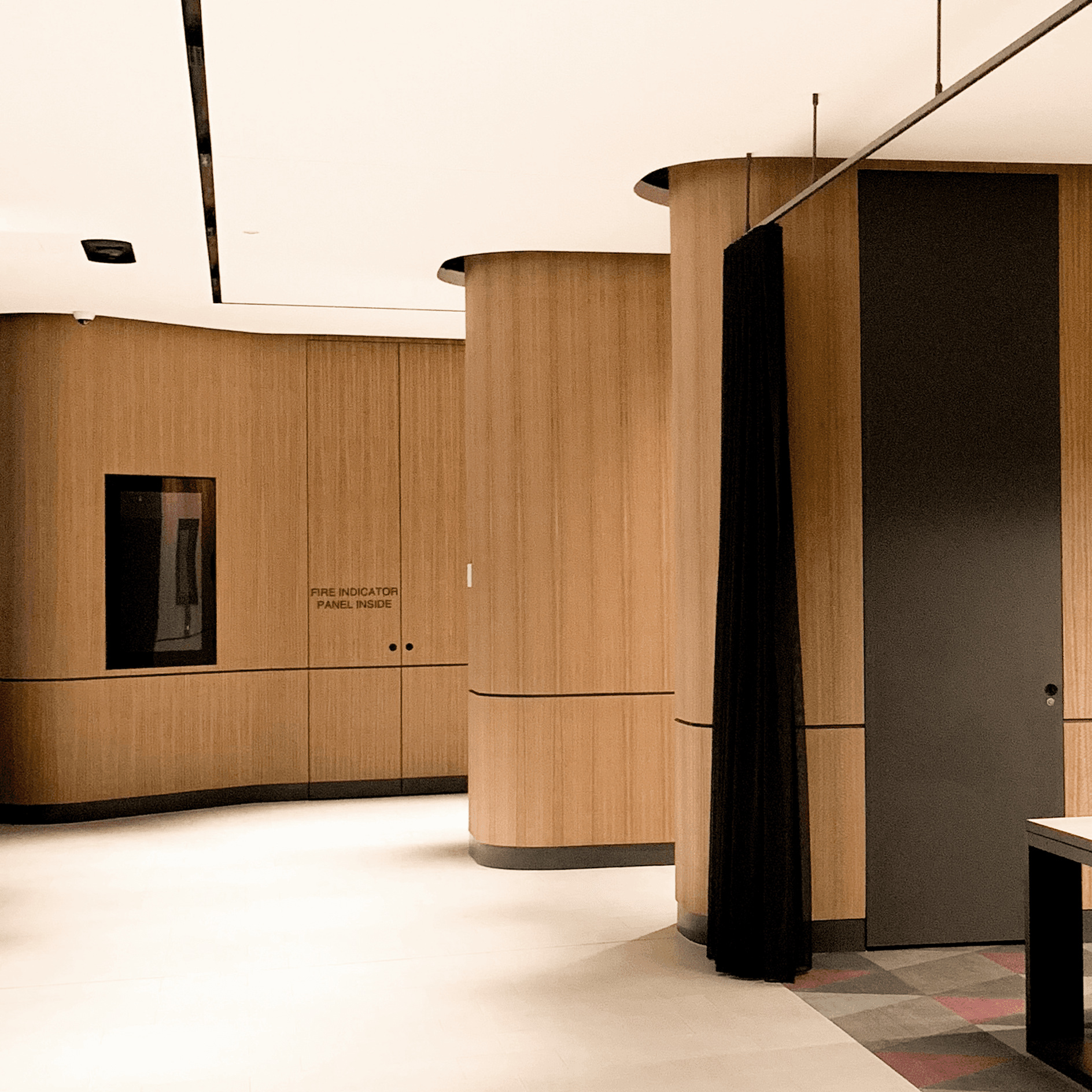 Curved timber-veneer walls and a black door in a Macquarie Park commercial lobby, with signage reading Fire Indicator Panel Inside
