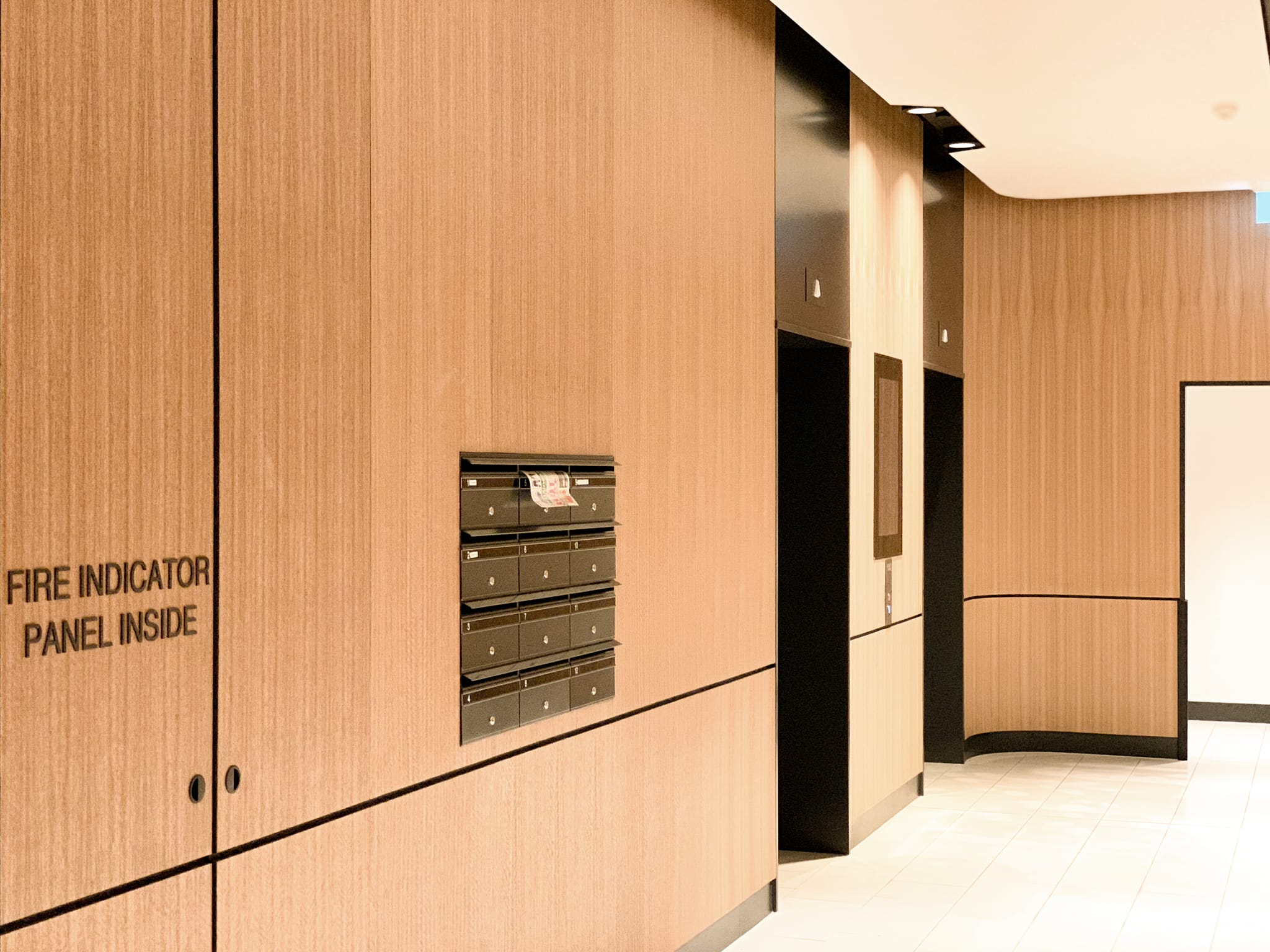 Recessed black tenant mailboxes set into a timber-clad wall beside the lift lobby, part of the Macquarie Park commercial interior