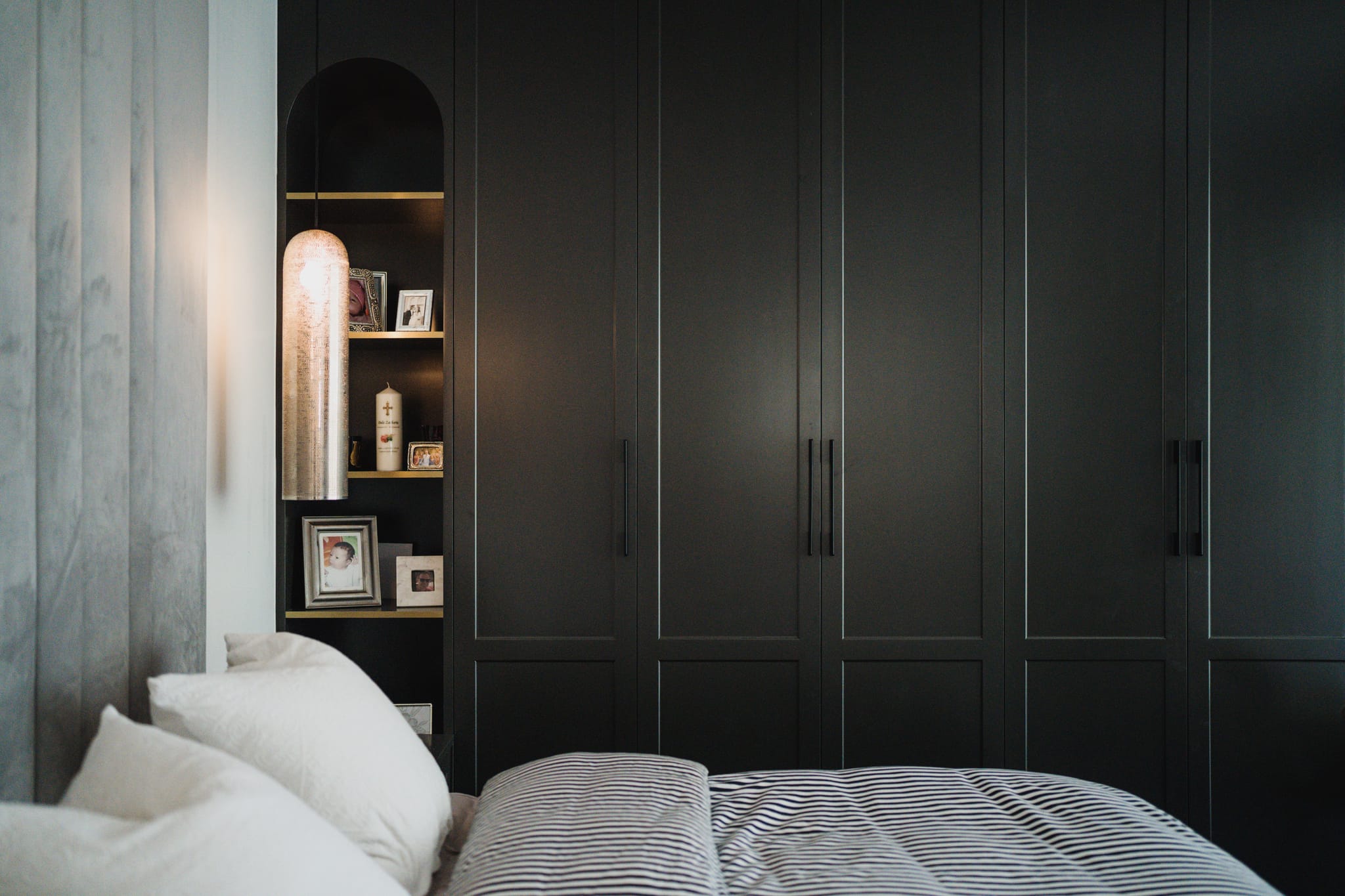 Bedroom with charcoal shaker wardrobes and an arched niche of framed photos, striped bedding and a woven pendant light in the Vaucluse family home.