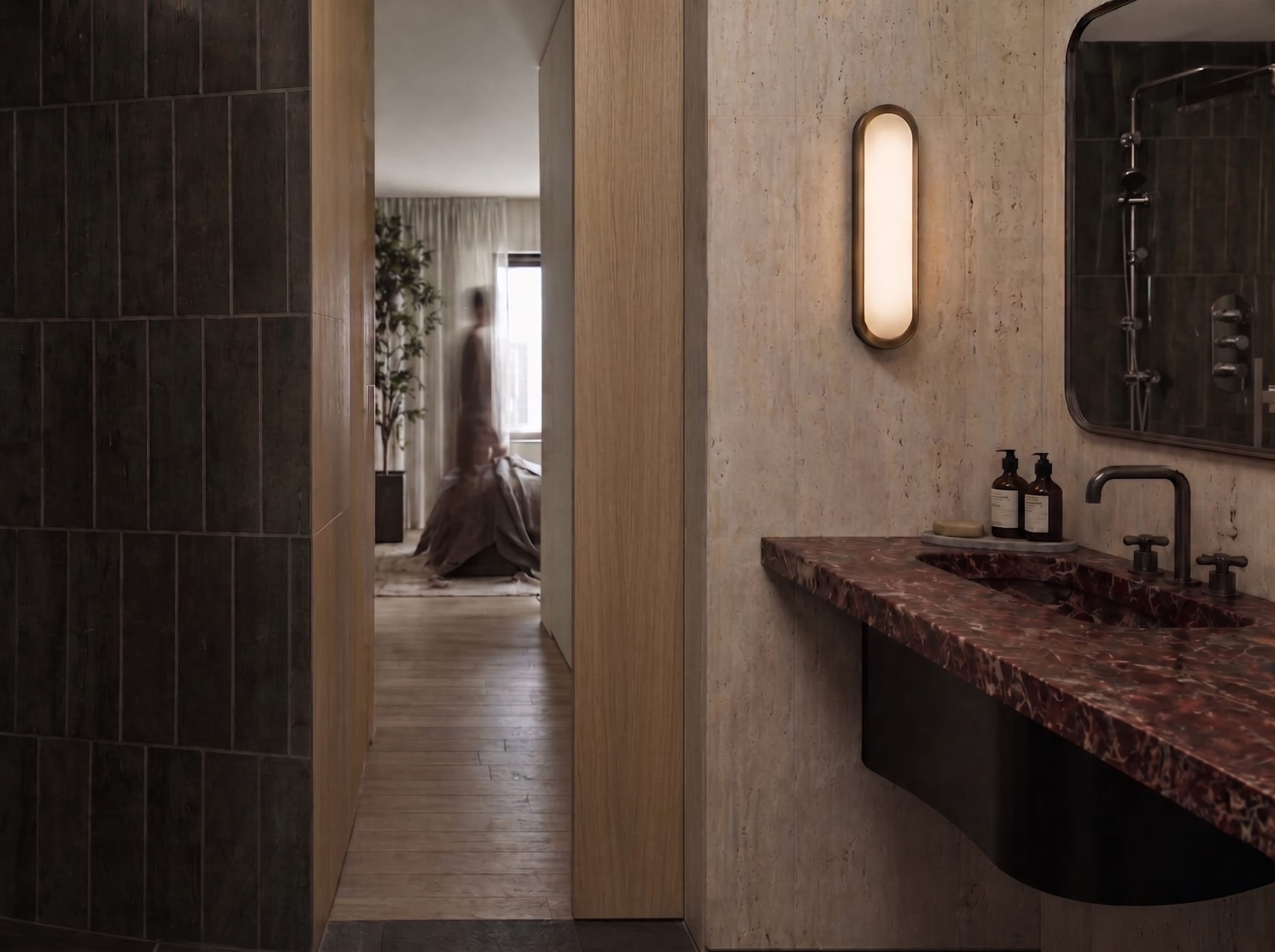 Ensuite with a burgundy marble vanity and aged-brass tapware, an oval sconce on travertine, opening to a timber-floored bedroom beyond