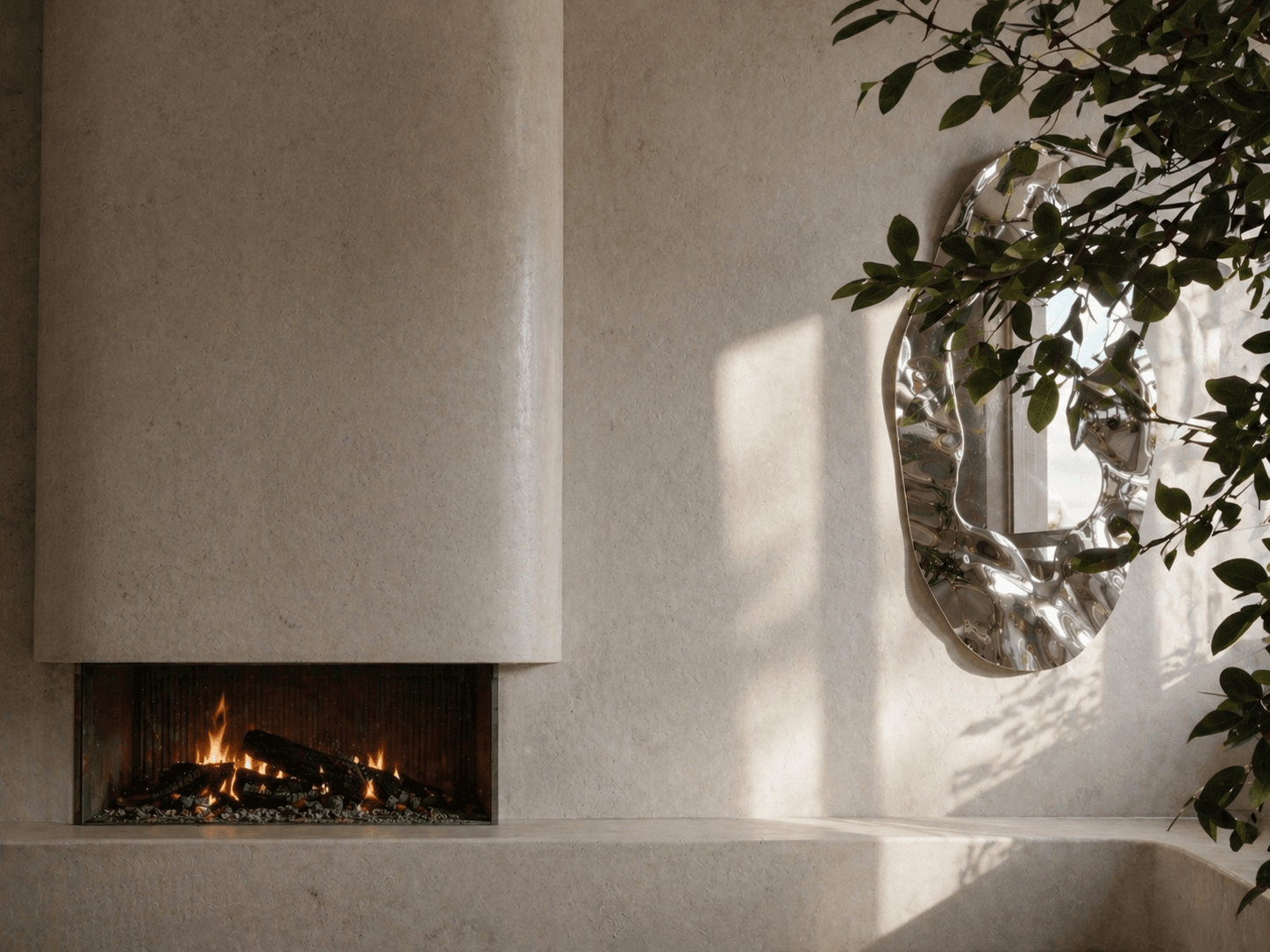 Pale natural stone fireplace with a lit fire beside a rippled polished-steel mirror, sunlight and foliage falling across the limestone wall